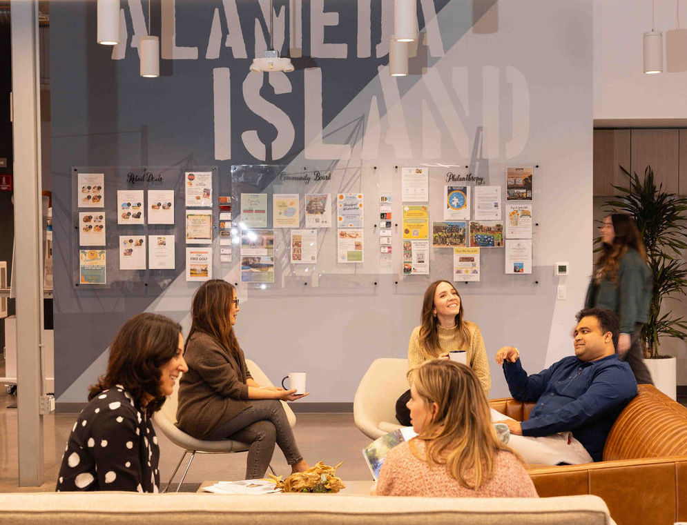 people sitting, smiling, and talking to one another in a lounge space with couches and chairs. 