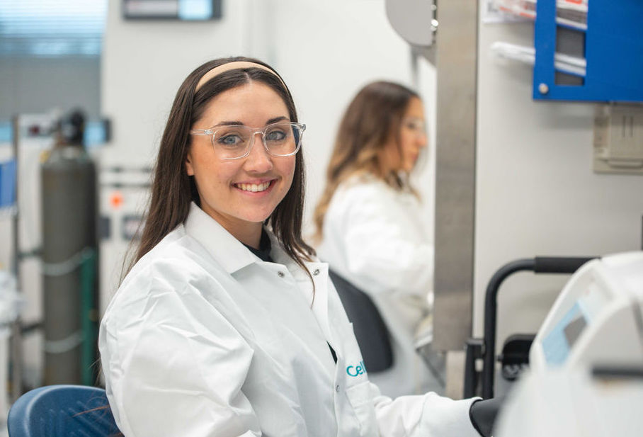 Smiling scientist in a CellFE lab coat sitting at a lab bench in lab.