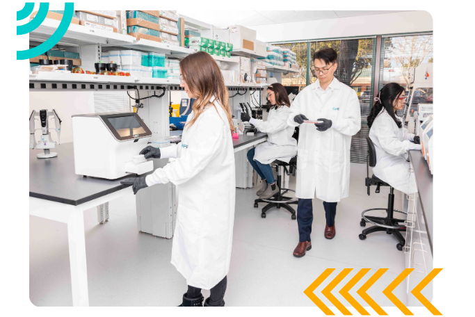 four scientists in CellFE lab coats working in a lab. The scientists at the front is using the Infinity MTx instrument.